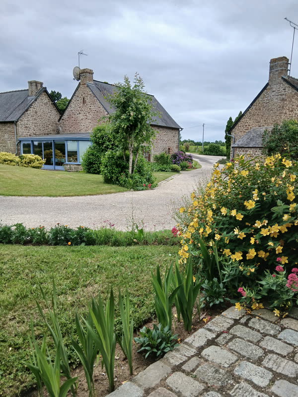 La longère en pierre et sa véranda vues depuis le jardin fleuri