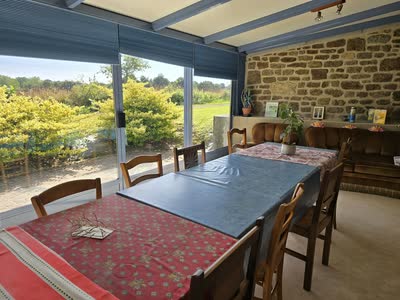 La véranda et son mur en pierre apparente, tables, banquettes et baies vitrées