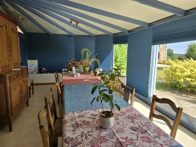 La véranda avec sa longue table dressée, ses stores bleus et la vue sur le jardin