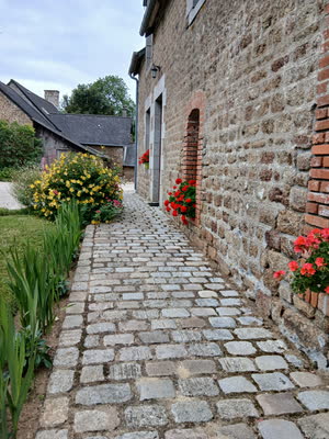 L'allée pavée de granit longeant un mur en pierre orné de géraniums rouges