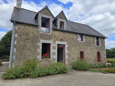 La façade en pierre du gîte, ses lucarnes à encadrements de granit et ses géraniums rouges