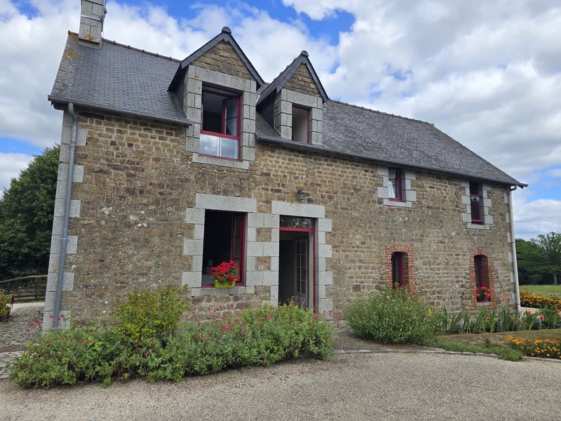 La façade en pierre du gîte, ses lucarnes à encadrements de granit et ses géraniums rouges