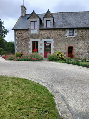 La façade en pierre à deux lucarnes et menuiseries rouges, devant un massif de valérianes roses