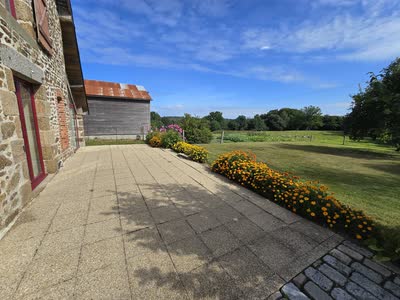 La terrasse dallée du gîte le long de la façade en pierre, ouverte sur la campagne