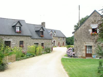 L'allée du hameau de Aussé bordée de bâtiments en pierre fleuris d'hortensias