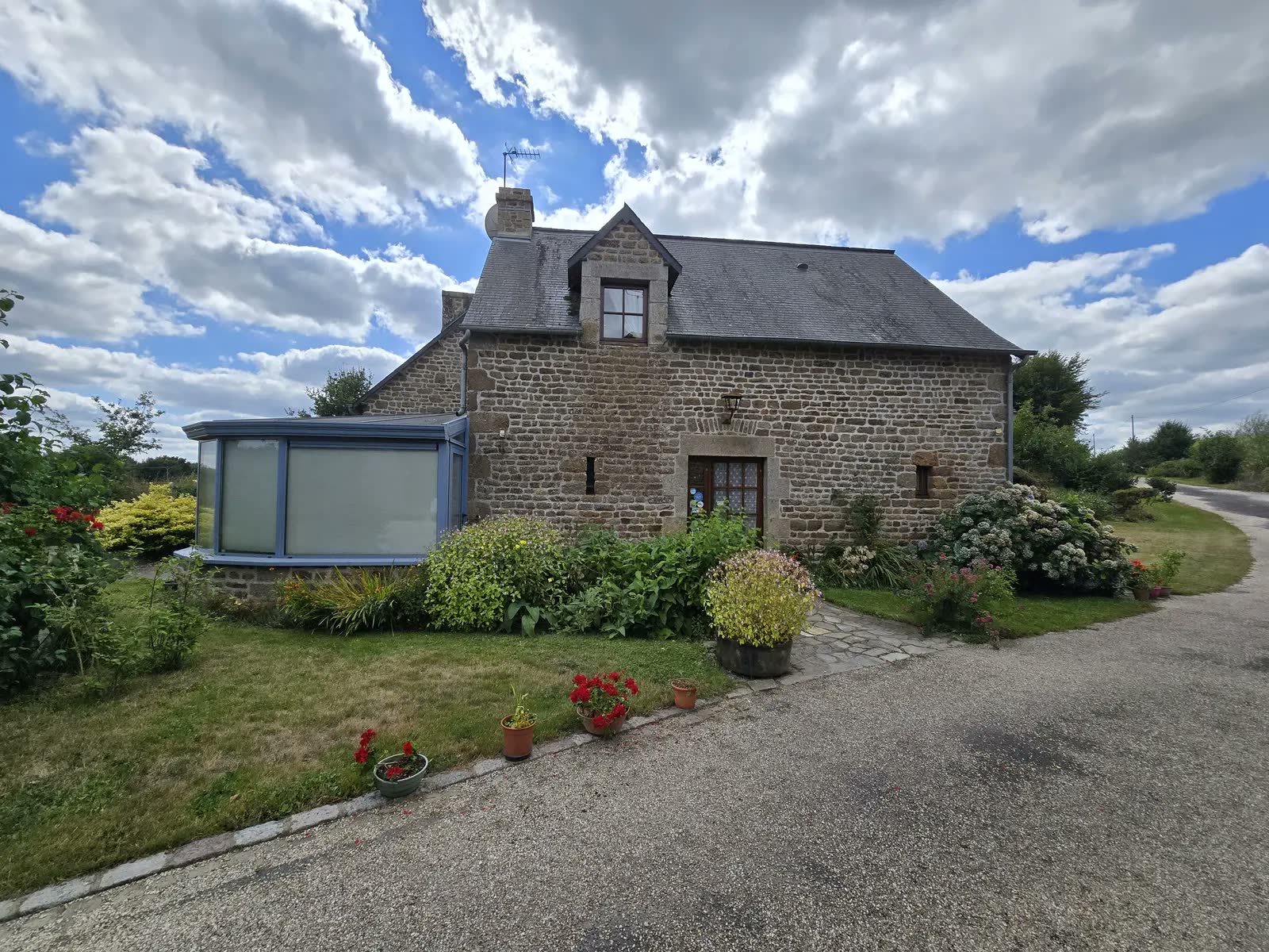 La longère en pierre des chambres d'hôtes de Aussé et sa véranda bleue, entourée de massifs fleuris